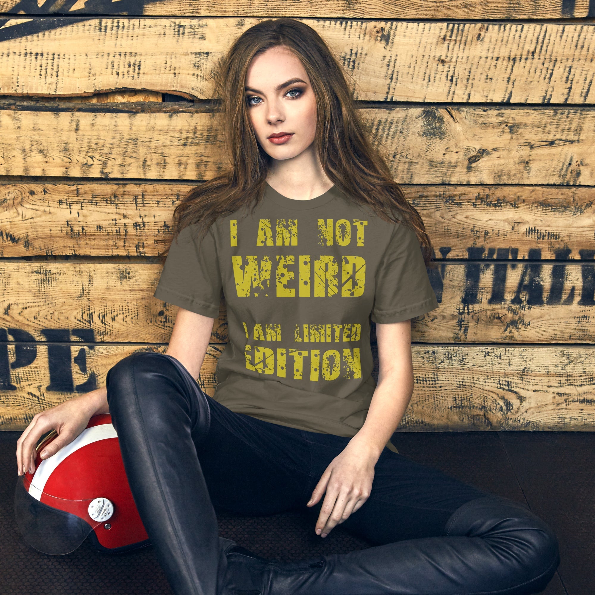 Unisex t-shirt with "I Am Not Weird, I Am Limited Edition" yellow text design, worn by a seated model against a rustic wooden background.