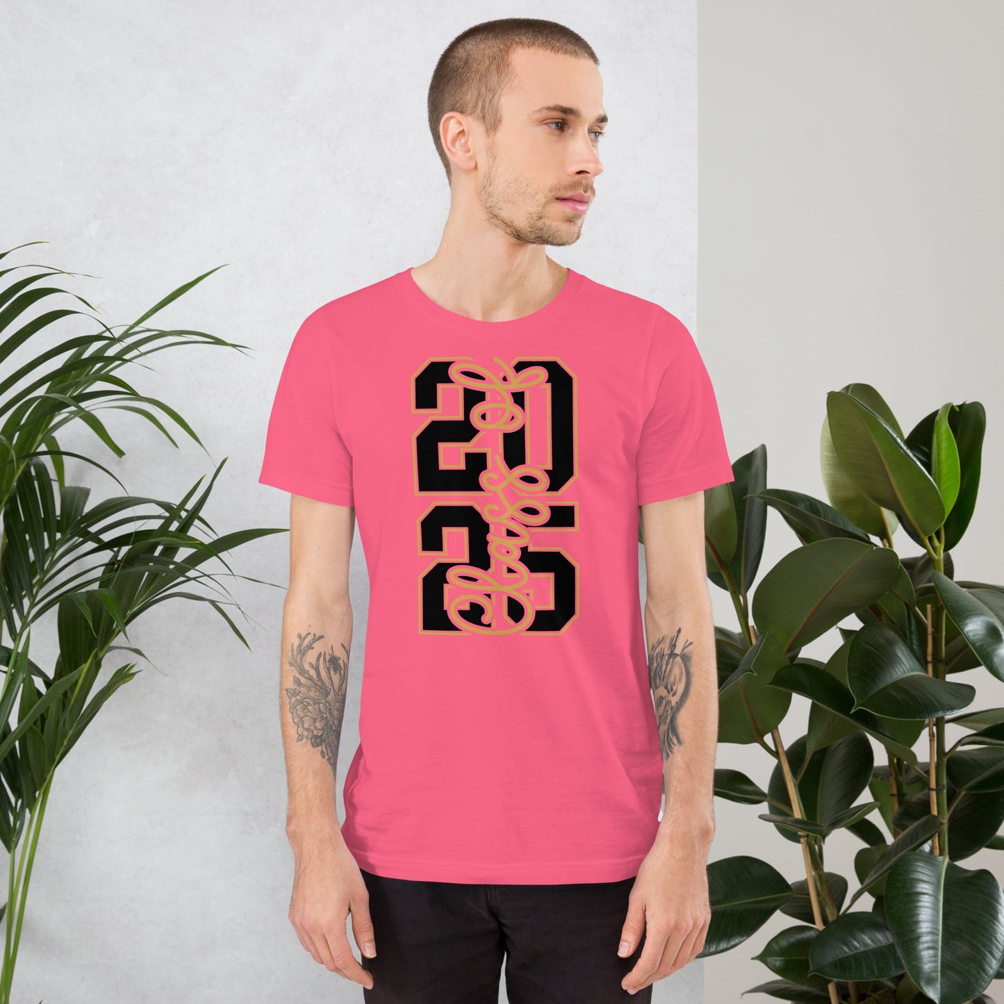 Class of 2026 vertical unisex t-shirt in pink worn by a person standing near plants.