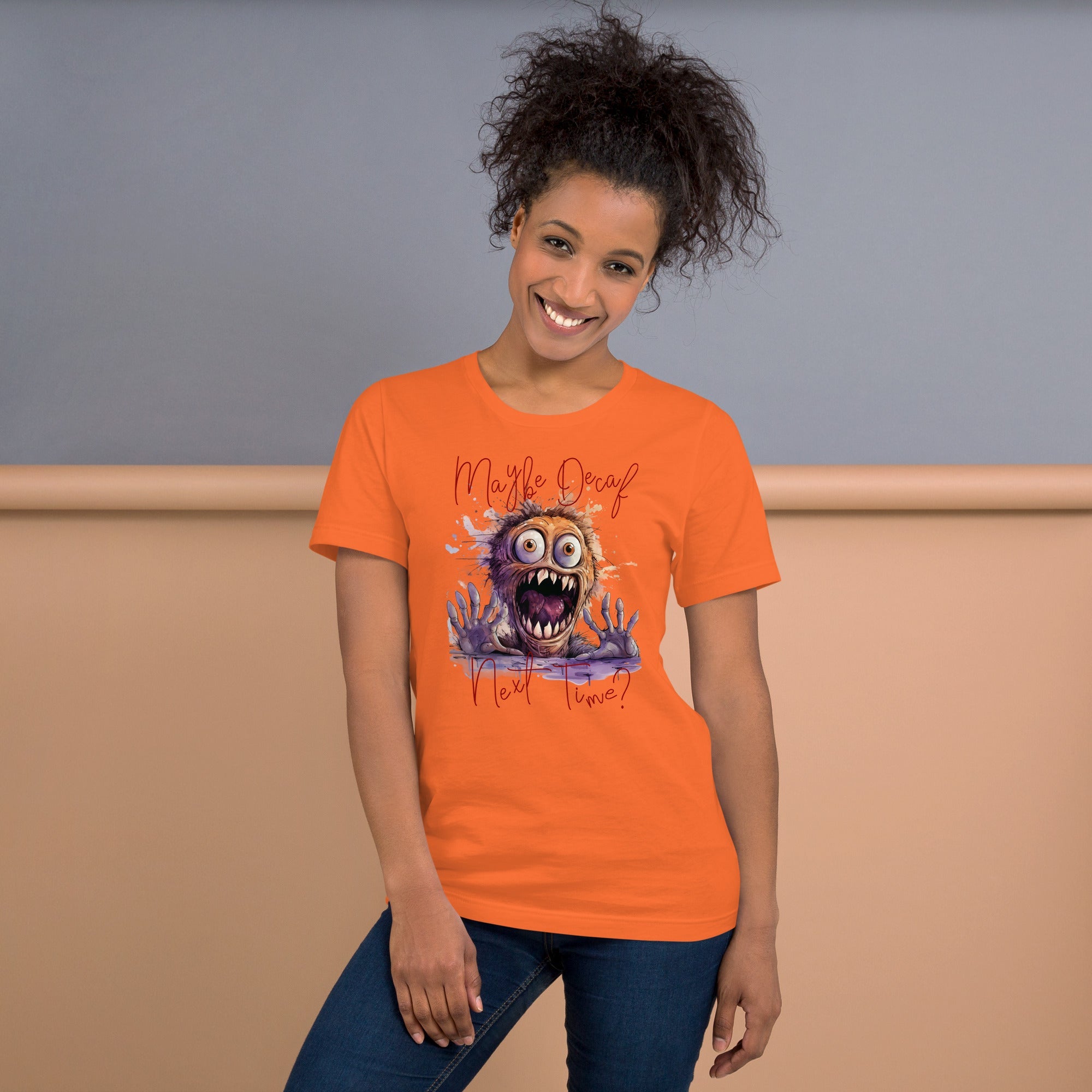Unisex t-shirt with humorous monster design and "Perhaps Decaf Next Time?" text, worn by smiling woman.