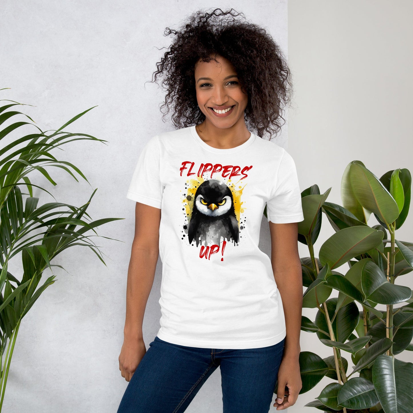 Unisex t-shirt with "Flippers Up" design featuring a playful penguin graphic, worn by a smiling person standing indoors.