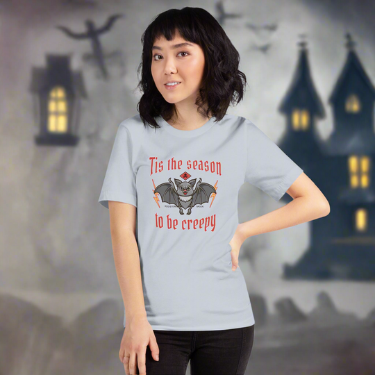 Unisex t-shirt with Halloween vampire design, themed "Tis the Season to Be Creepy," modeled in front of haunted house backdrop.