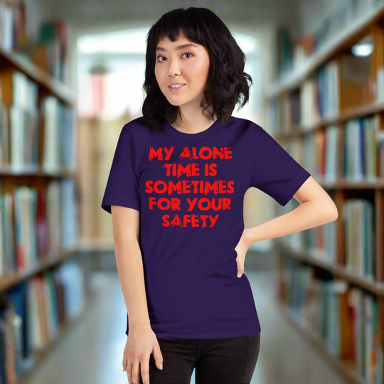 Unisex t-shirt with "My alone time is sometimes for your safety" text in red, worn by a person in a library.