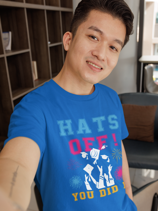 Graduation unisex t-shirt with "Hats Off! You did it" design in blue, worn by a smiling person indoors.