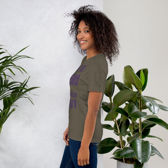 Unisex t-shirt with "I am not Weird" in purple text, worn by a smiling person, standing near plants.