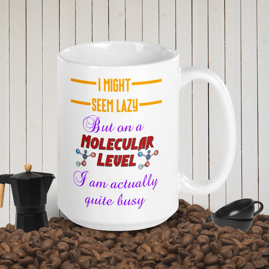 White glossy mug with humorous text about appearing lazy but being busy, surrounded by coffee beans and pot.