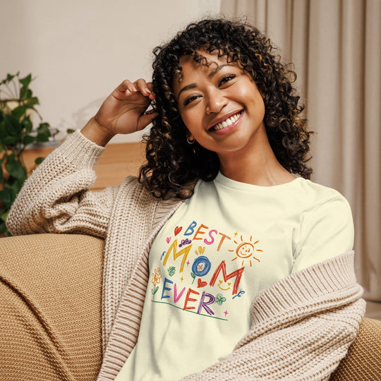 Woman smiling and wearing a "Best Mom Ever" relaxed t-shirt, paired with a cozy cardigan, seated in a comfortable indoor setting.